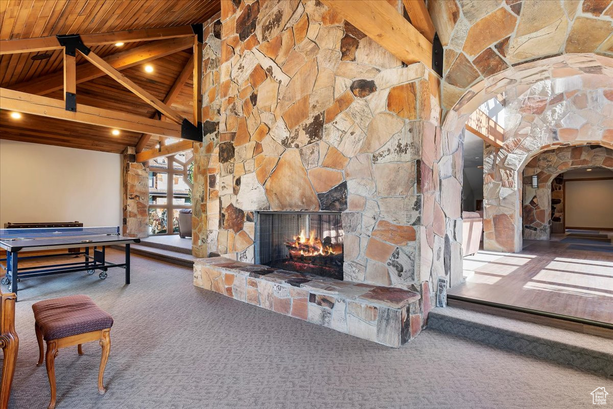 Carpeted living room with beam ceiling, high vaulted ceiling, a stone fireplace, and wood ceiling