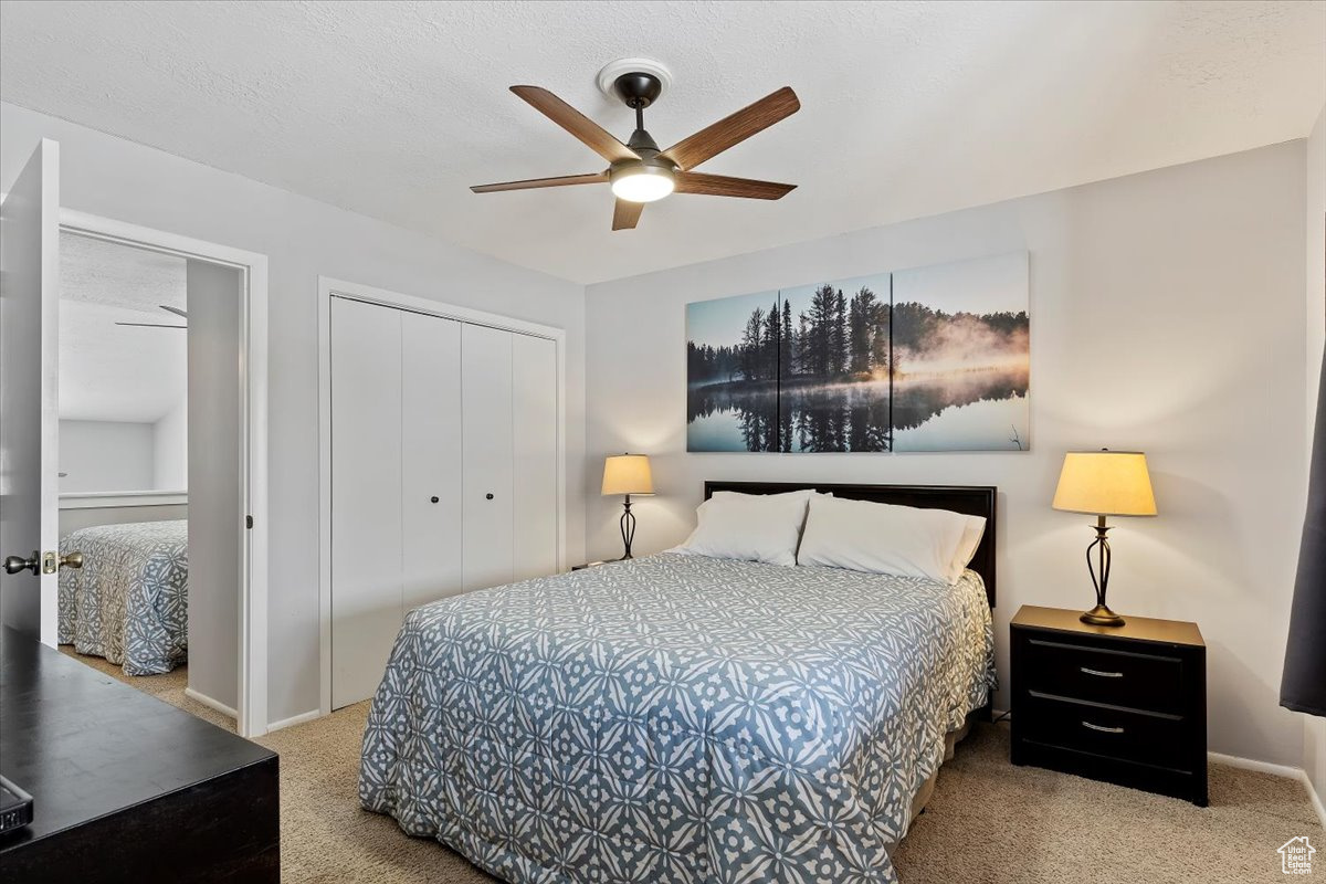 Carpeted bedroom featuring ceiling fan and a closet