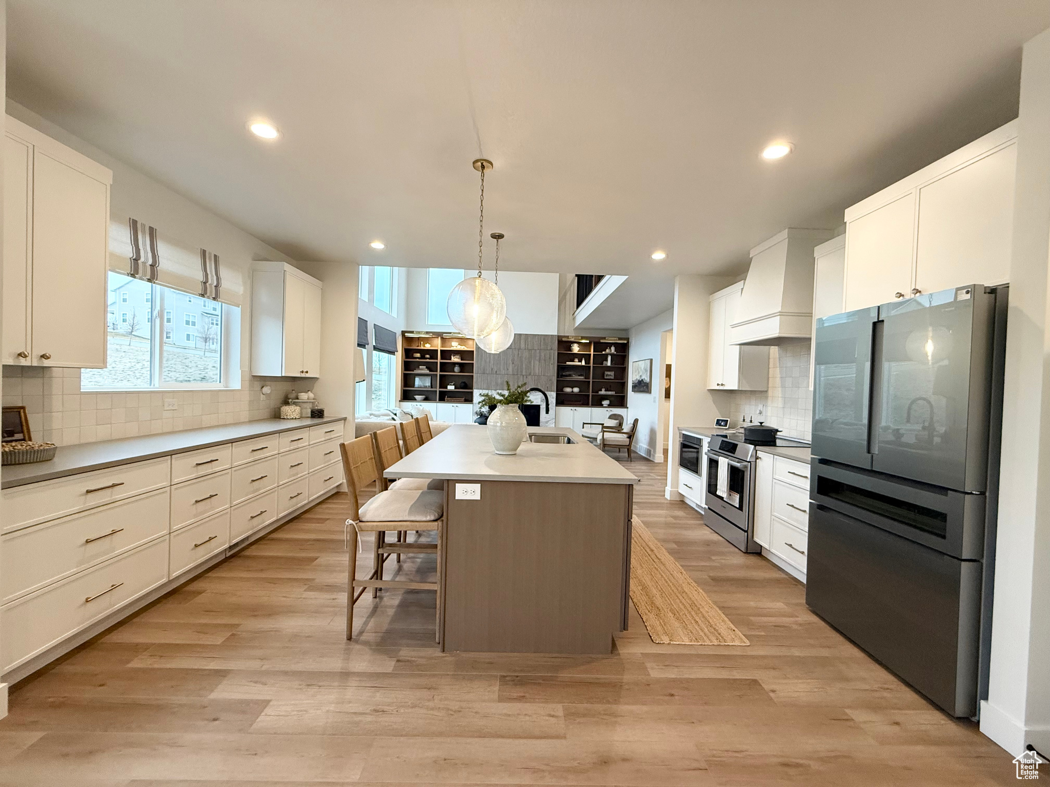 Kitchen featuring decorative light fixtures, a kitchen bar, a kitchen island with sink, appliances with stainless steel finishes, and light wood-type flooring