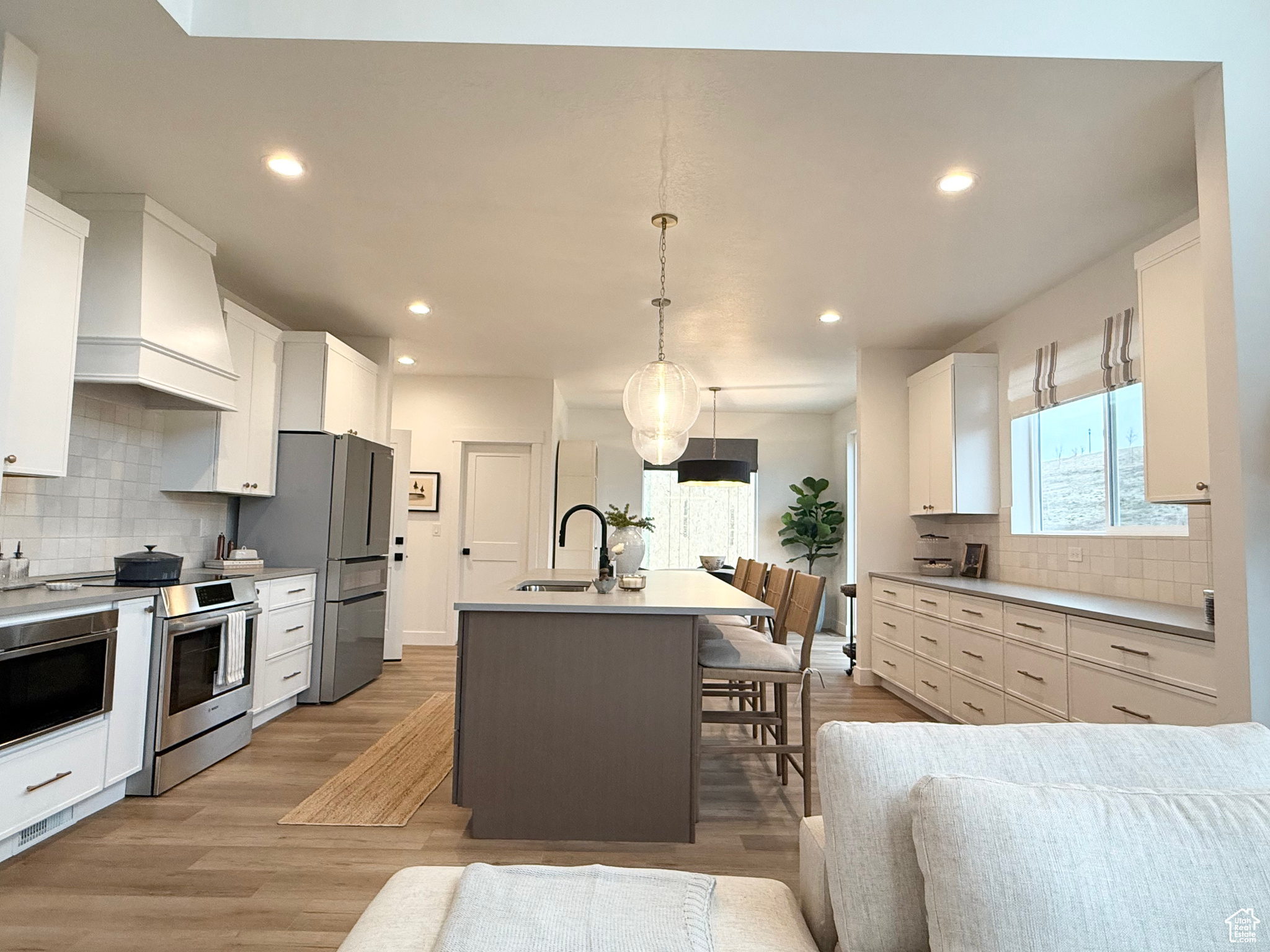 Kitchen with white cabinets, pendant lighting, stainless steel appliances, and an island with sink