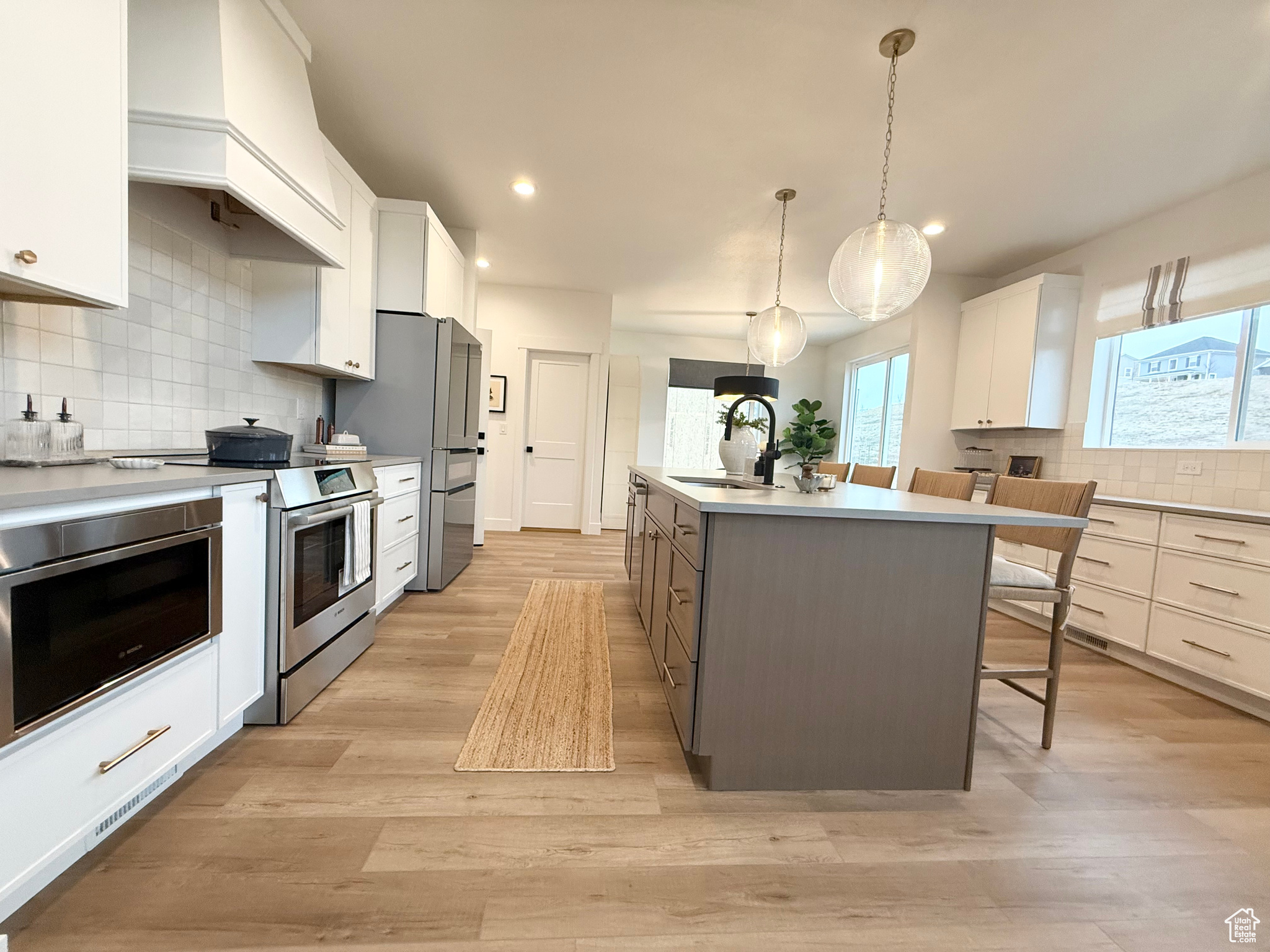 Kitchen featuring a kitchen island with sink, white cabinets, sink, hanging light fixtures, and stainless steel appliances