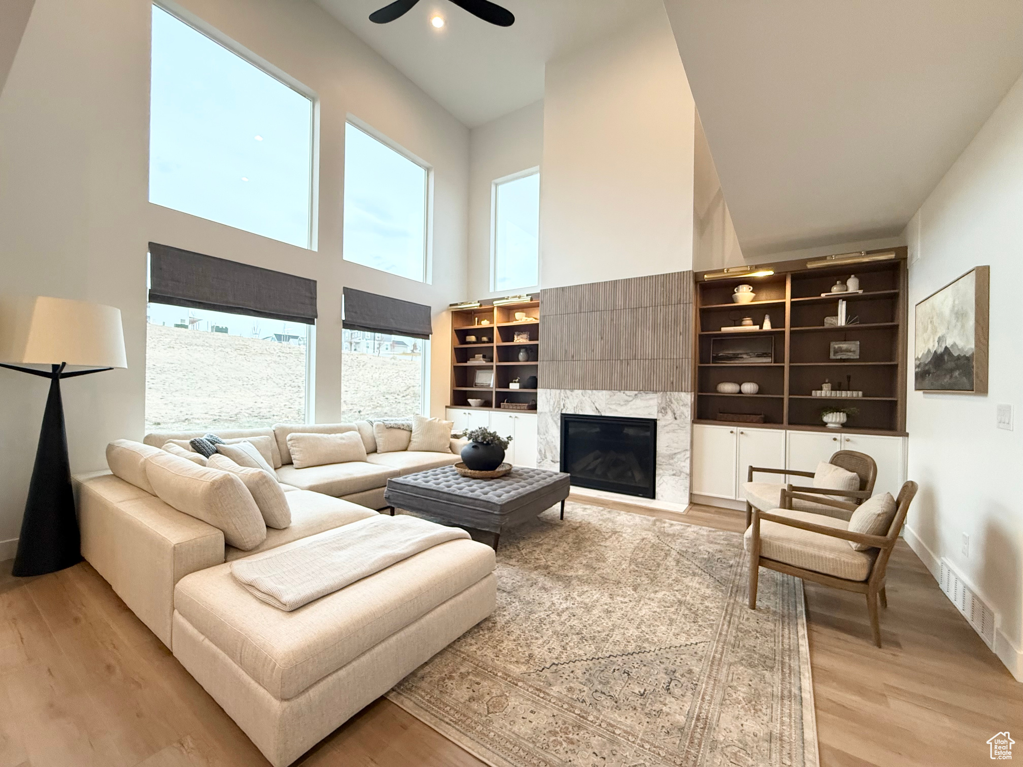 Living room with ceiling fan, a high ceiling, a high end fireplace, and light hardwood / wood-style flooring