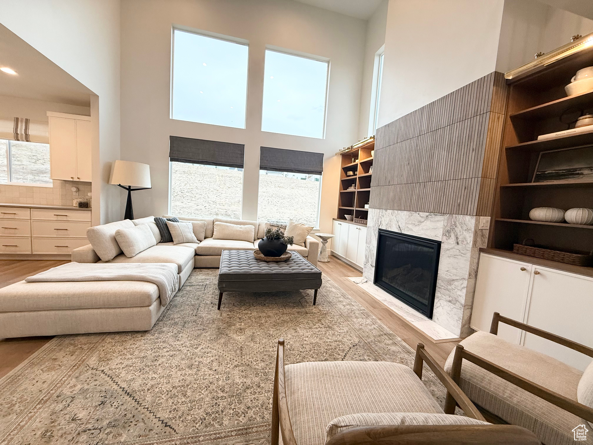 Living room featuring light wood-type flooring, a high ceiling, and a high end fireplace