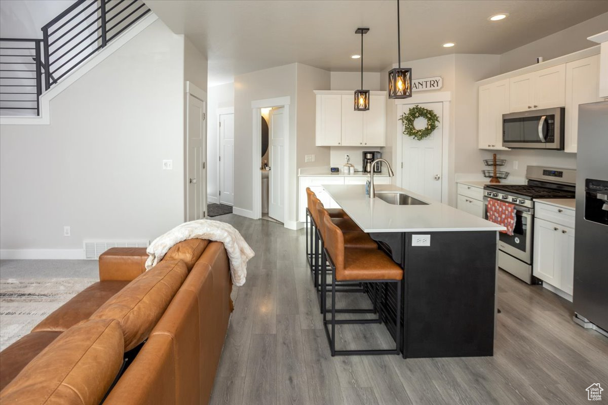 Kitchen featuring white cabinetry, sink, stainless steel appliances, and a center island with sink