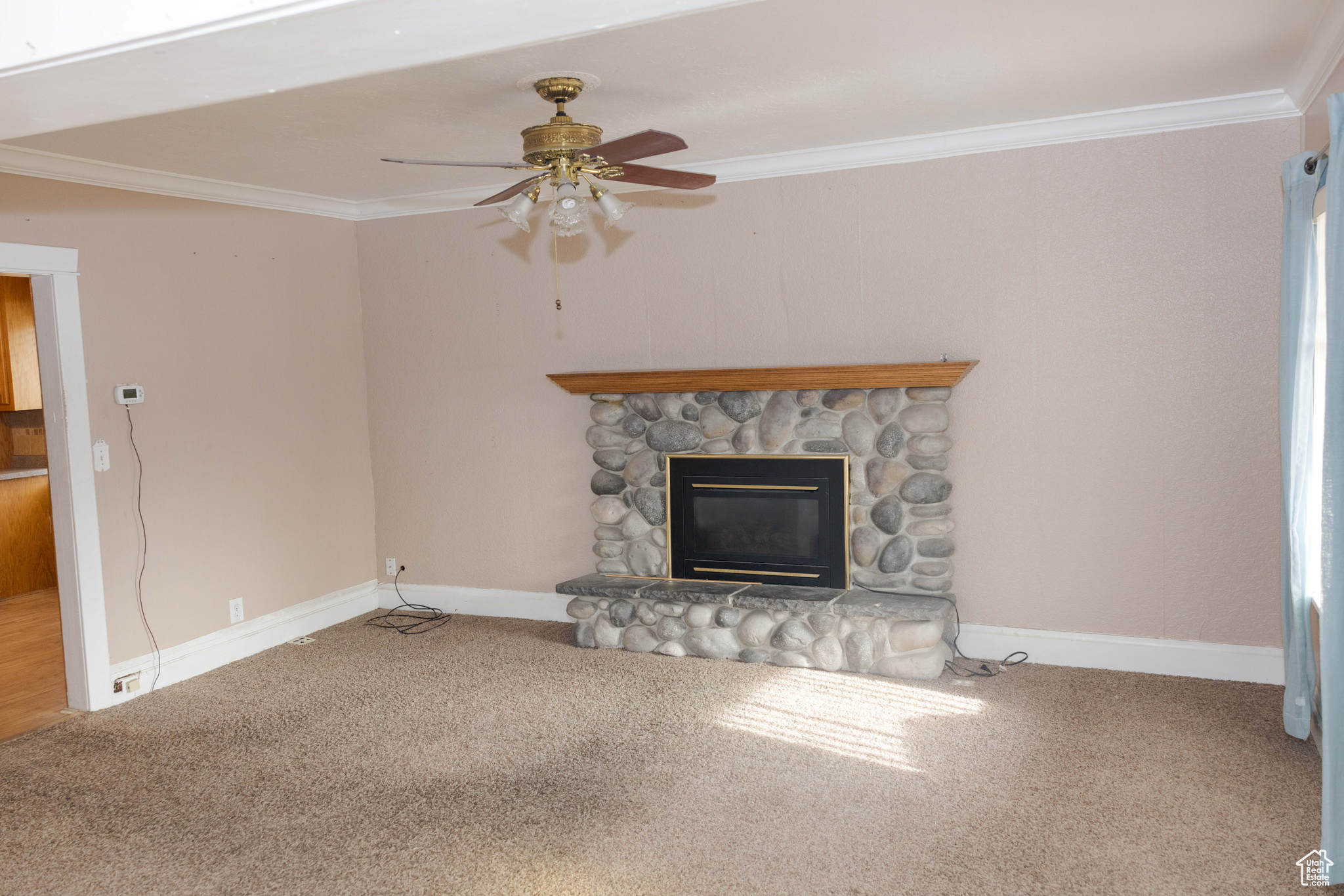 Unfurnished living room with carpet floors, a stone fireplace, crown molding, and ceiling fan