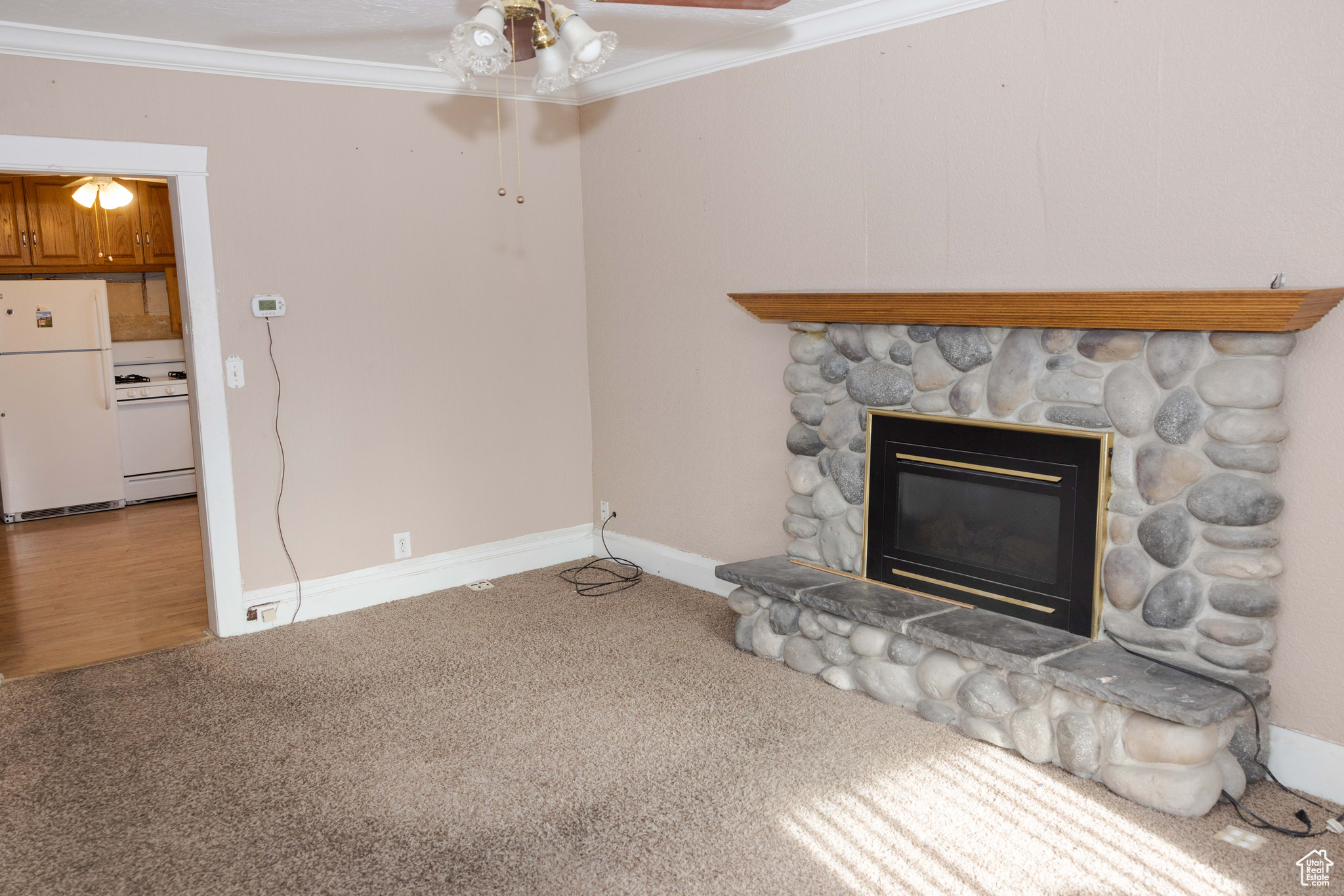 Unfurnished living room with carpet, ceiling fan, a stone fireplace, and crown molding