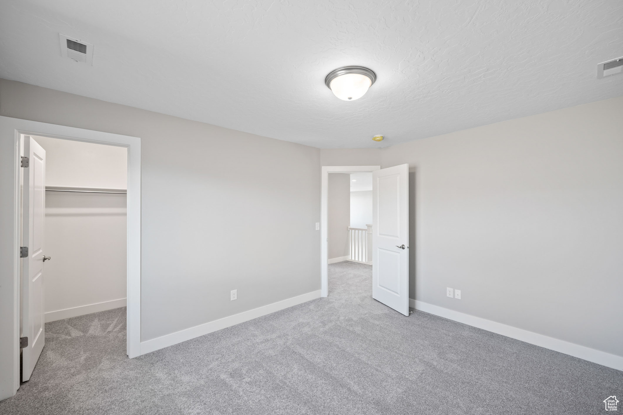 Unfurnished bedroom with a textured ceiling, a walk in closet, light carpet, and a closet