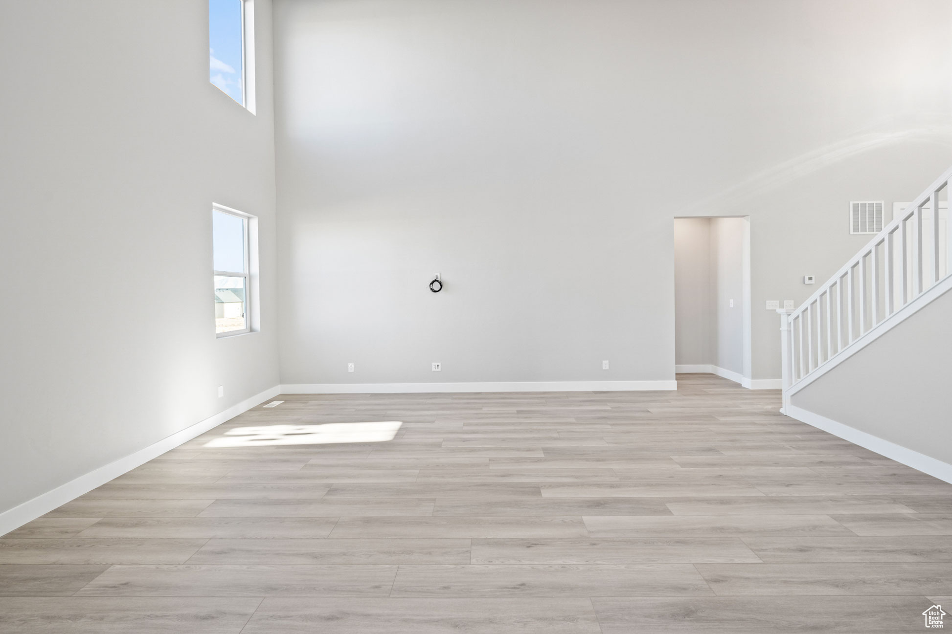 Unfurnished living room featuring a healthy amount of sunlight, a towering ceiling, and light hardwood / wood-style flooring