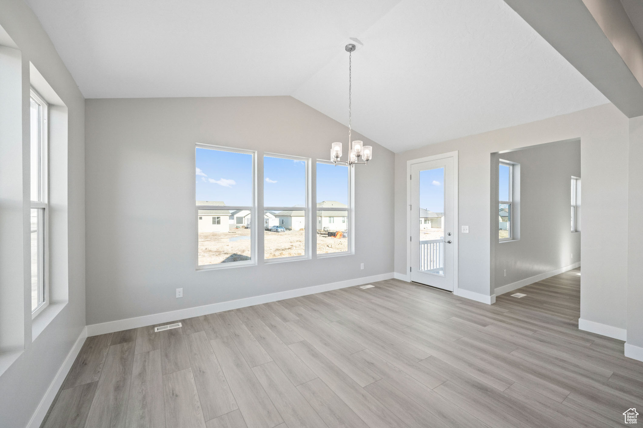 Unfurnished dining area with light hardwood / wood-style floors, vaulted ceiling, and an inviting chandelier