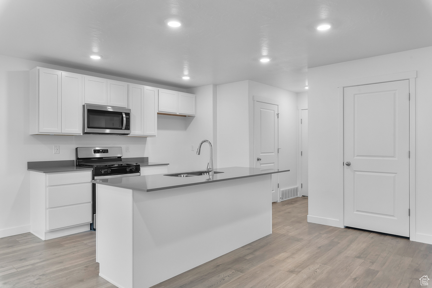 Kitchen featuring white cabinets, appliances with stainless steel finishes, an island with sink, and sink