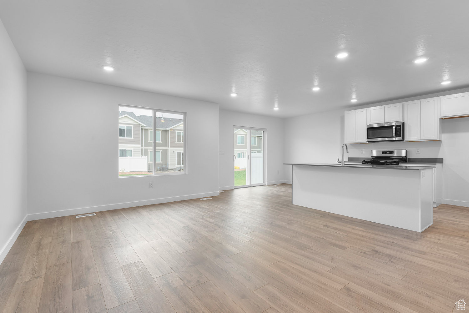 Kitchen featuring white cabinetry, sink, light hardwood / wood-style floors, a center island with sink, and appliances with stainless steel finishes