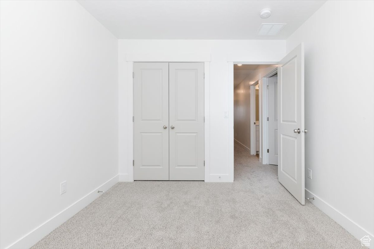 Unfurnished bedroom featuring light carpet and a closet