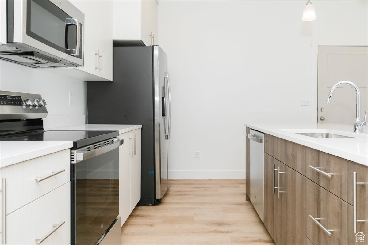 Kitchen featuring white cabinets, sink, hanging light fixtures, light hardwood / wood-style flooring, and stainless steel appliances