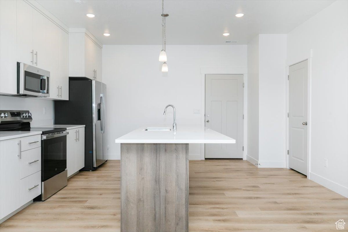 Kitchen with stainless steel appliances, sink, pendant lighting, a center island with sink, and white cabinetry