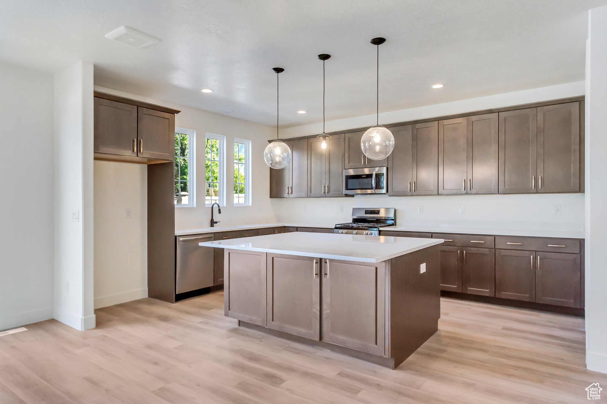 Kitchen featuring appliances with stainless steel finishes, light wood-type flooring, sink, decorative light fixtures, and a kitchen island