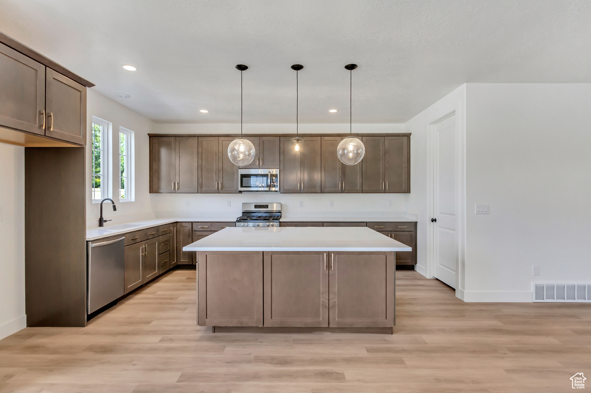 Kitchen featuring pendant lighting, sink, light wood-type flooring, appliances with stainless steel finishes, and a kitchen island