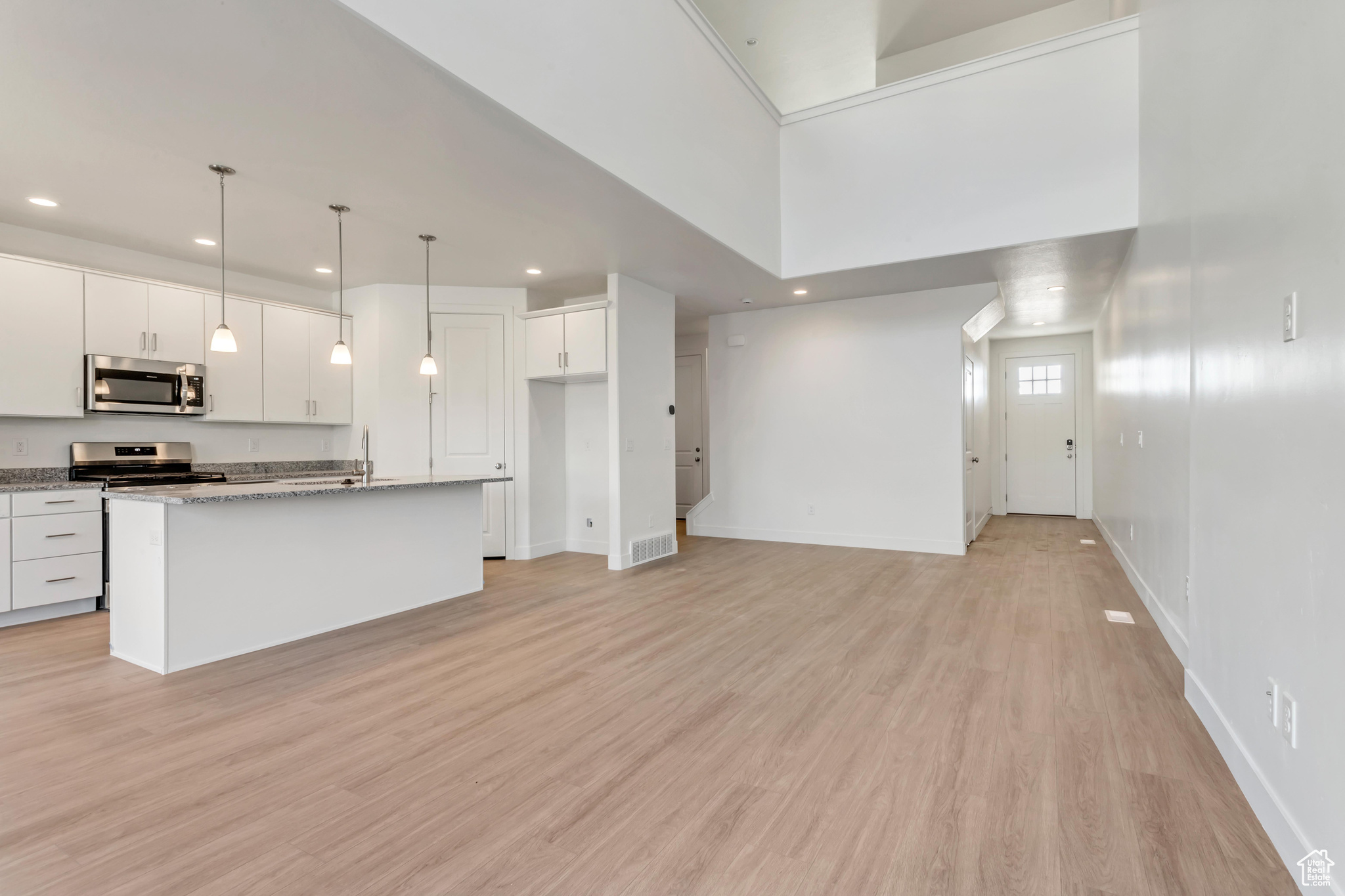 Kitchen featuring white cabinets, pendant lighting, stainless steel appliances, and a kitchen island with sink