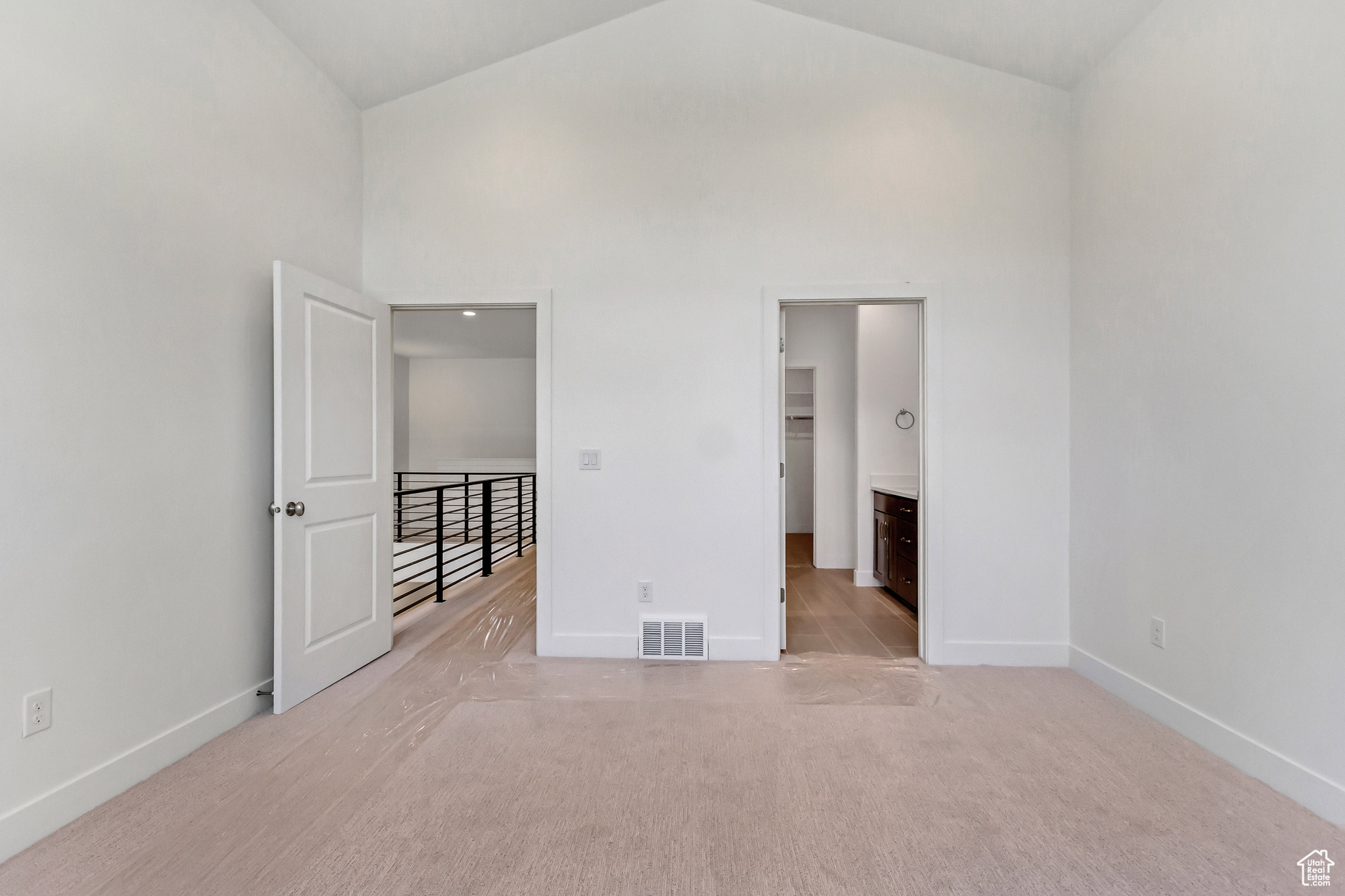 Unfurnished bedroom featuring light colored carpet, a spacious closet, high vaulted ceiling, and connected bathroom