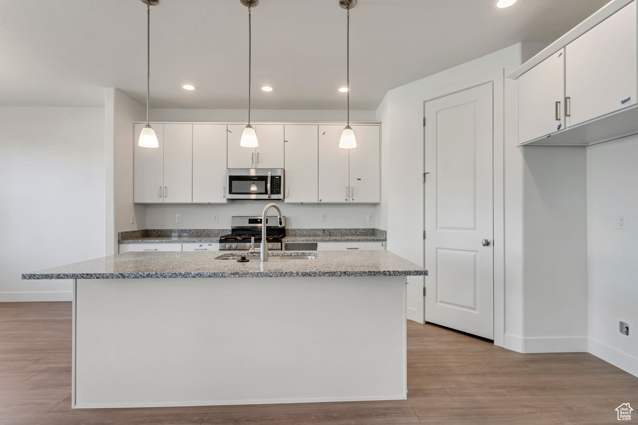 Kitchen featuring white cabinets, decorative light fixtures, and appliances with stainless steel finishes