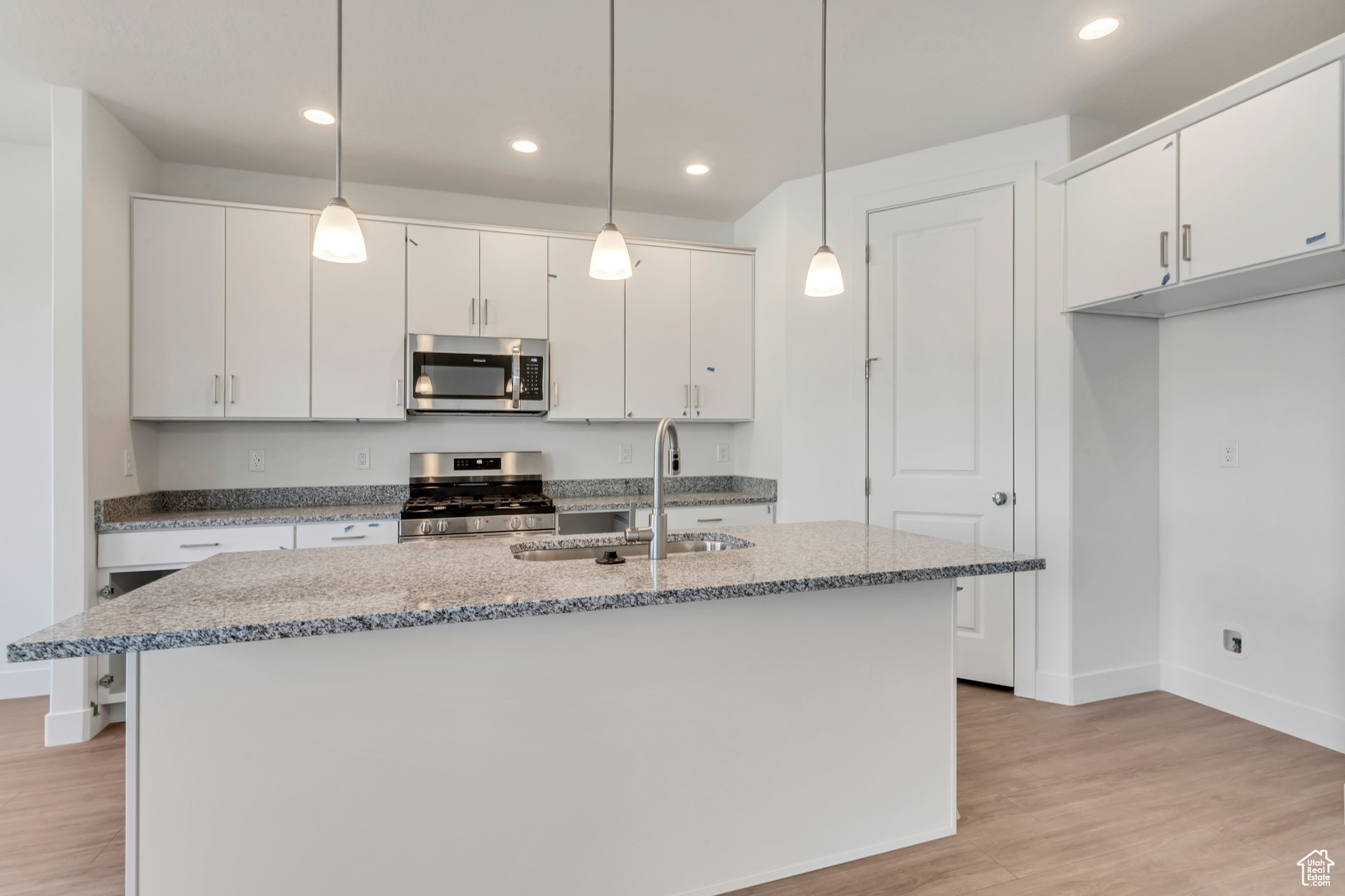 Kitchen with white cabinets, pendant lighting, stainless steel appliances, and sink