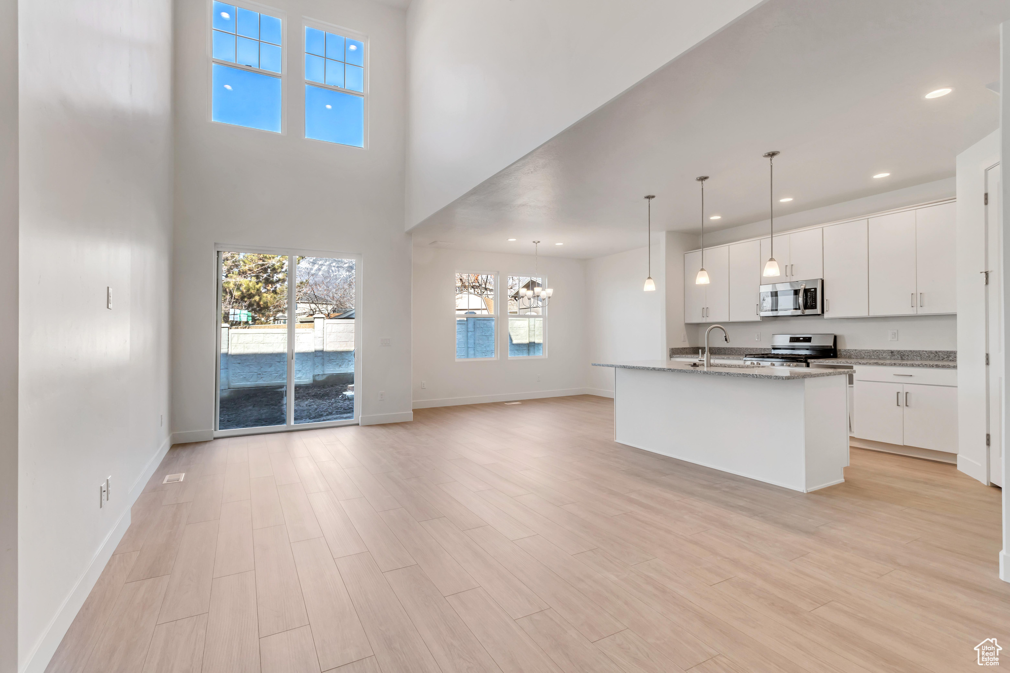 Kitchen featuring white cabinets, light stone countertops, an island with sink, decorative light fixtures, and stainless steel appliances