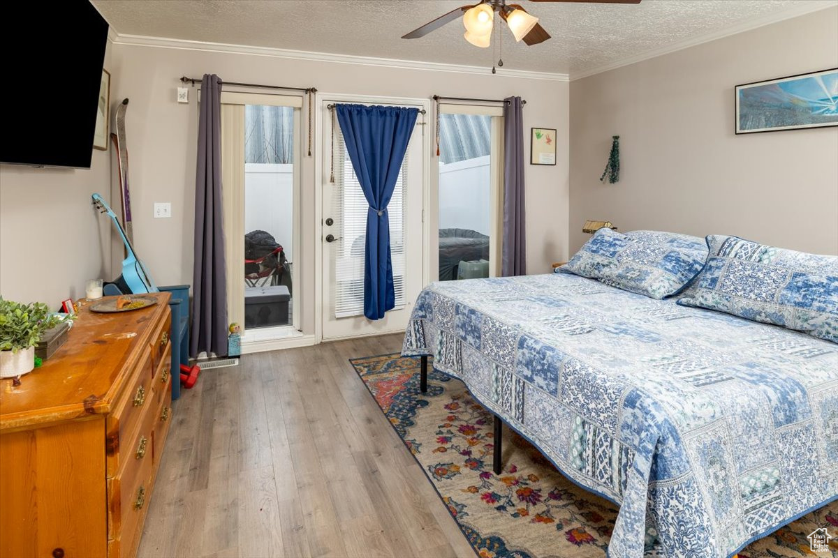 Bedroom with ceiling fan, light hardwood / wood-style flooring, crown molding, and a textured ceiling