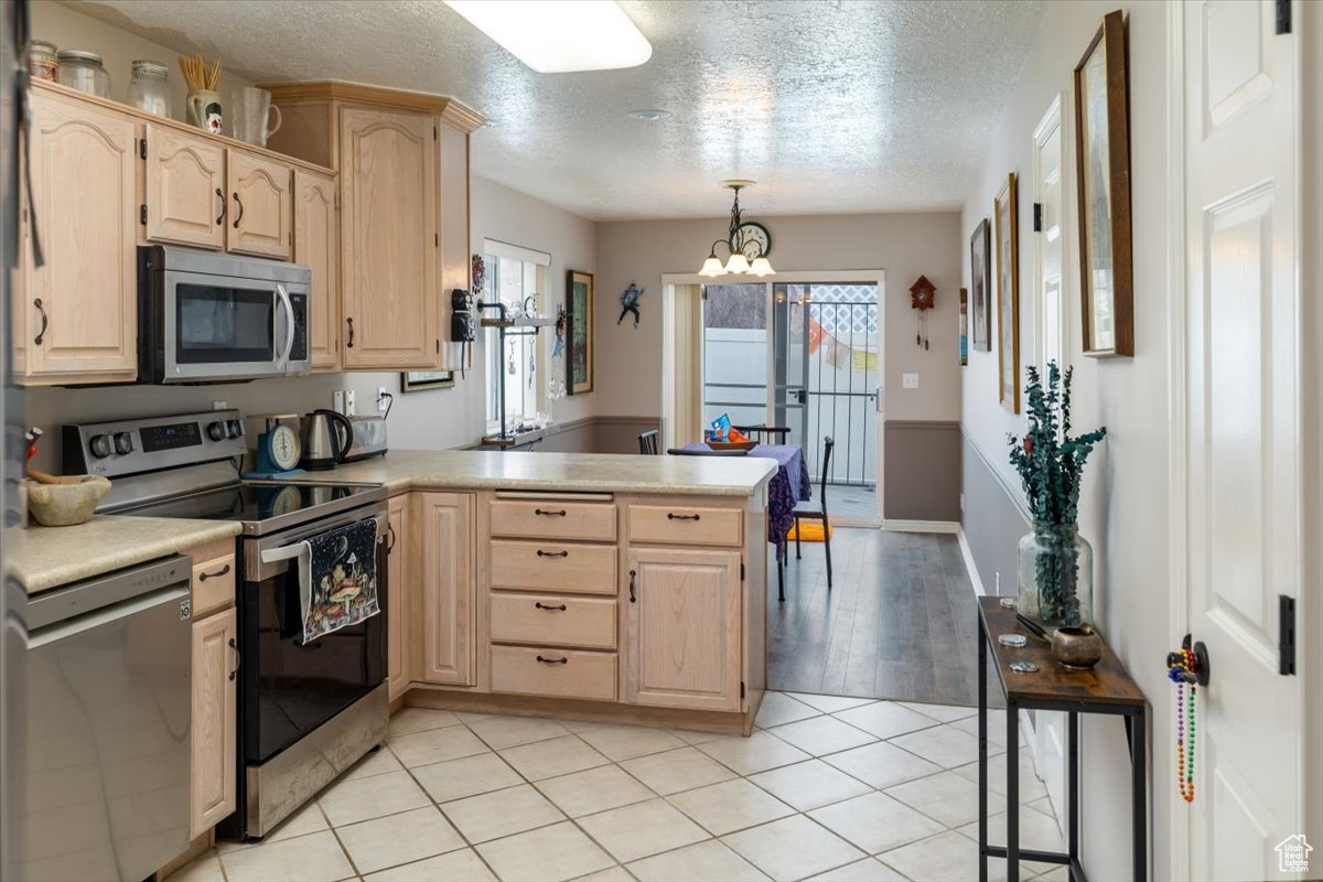 Kitchen featuring kitchen peninsula, light brown cabinetry, stainless steel appliances, a notable chandelier, and light tile patterned flooring