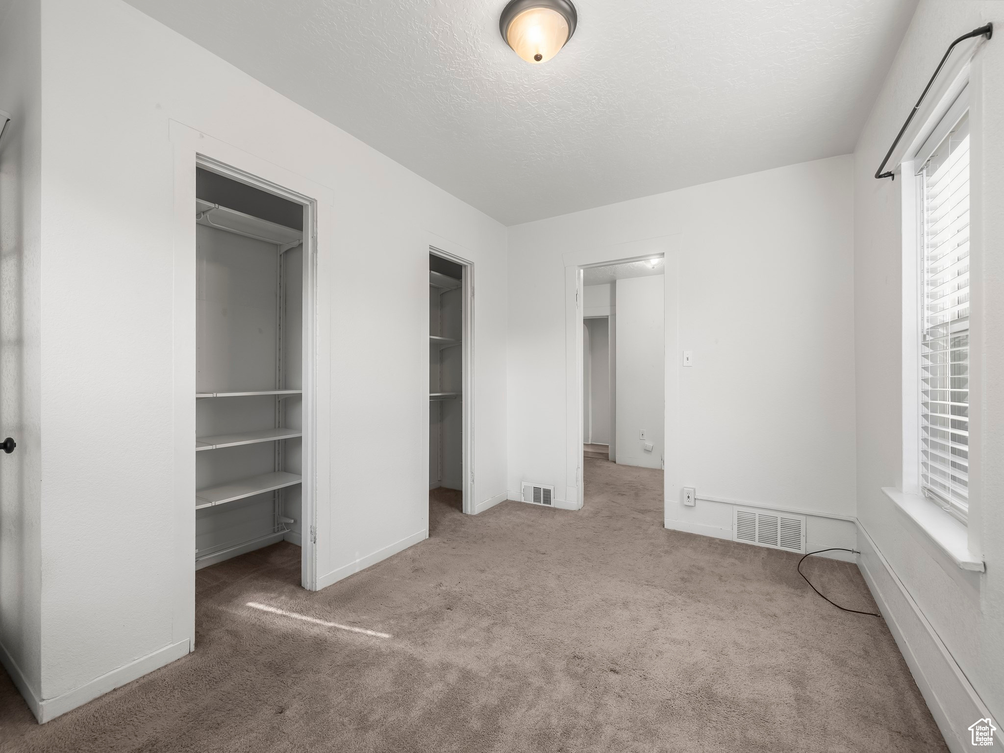 Unfurnished bedroom with light colored carpet, a walk in closet, and a textured ceiling