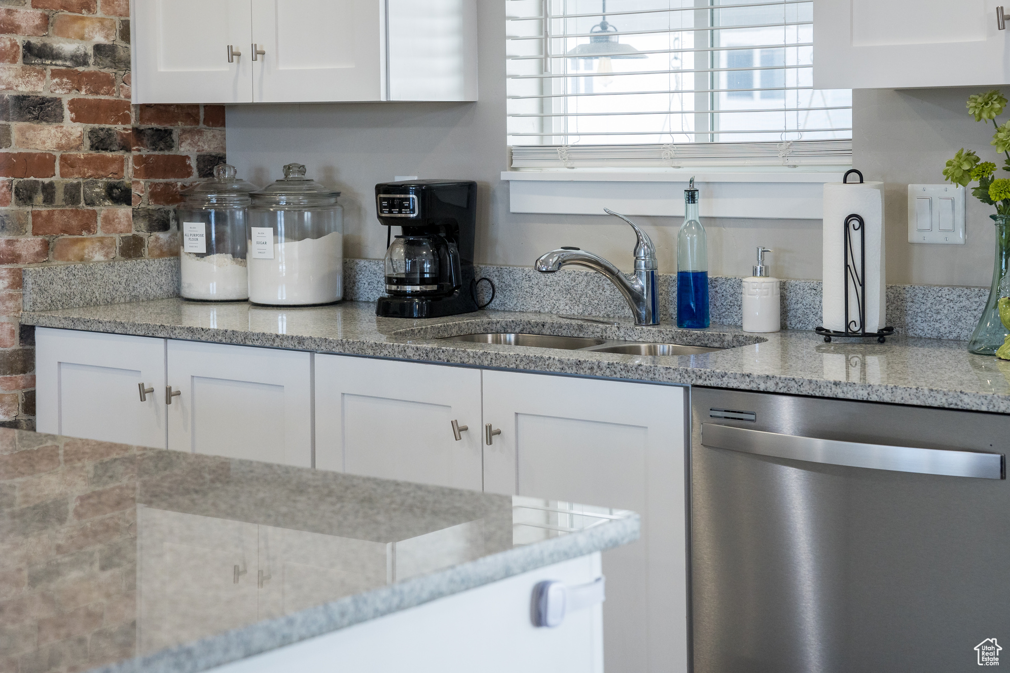 Kitchen featuring stainless steel dishwasher, sink, white cabinets, and light stone counters