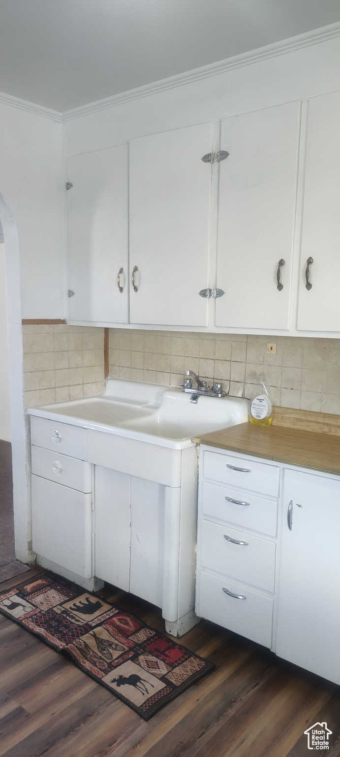 Kitchen featuring white cabinets, dark hardwood / wood-style flooring, ornamental molding, and backsplash