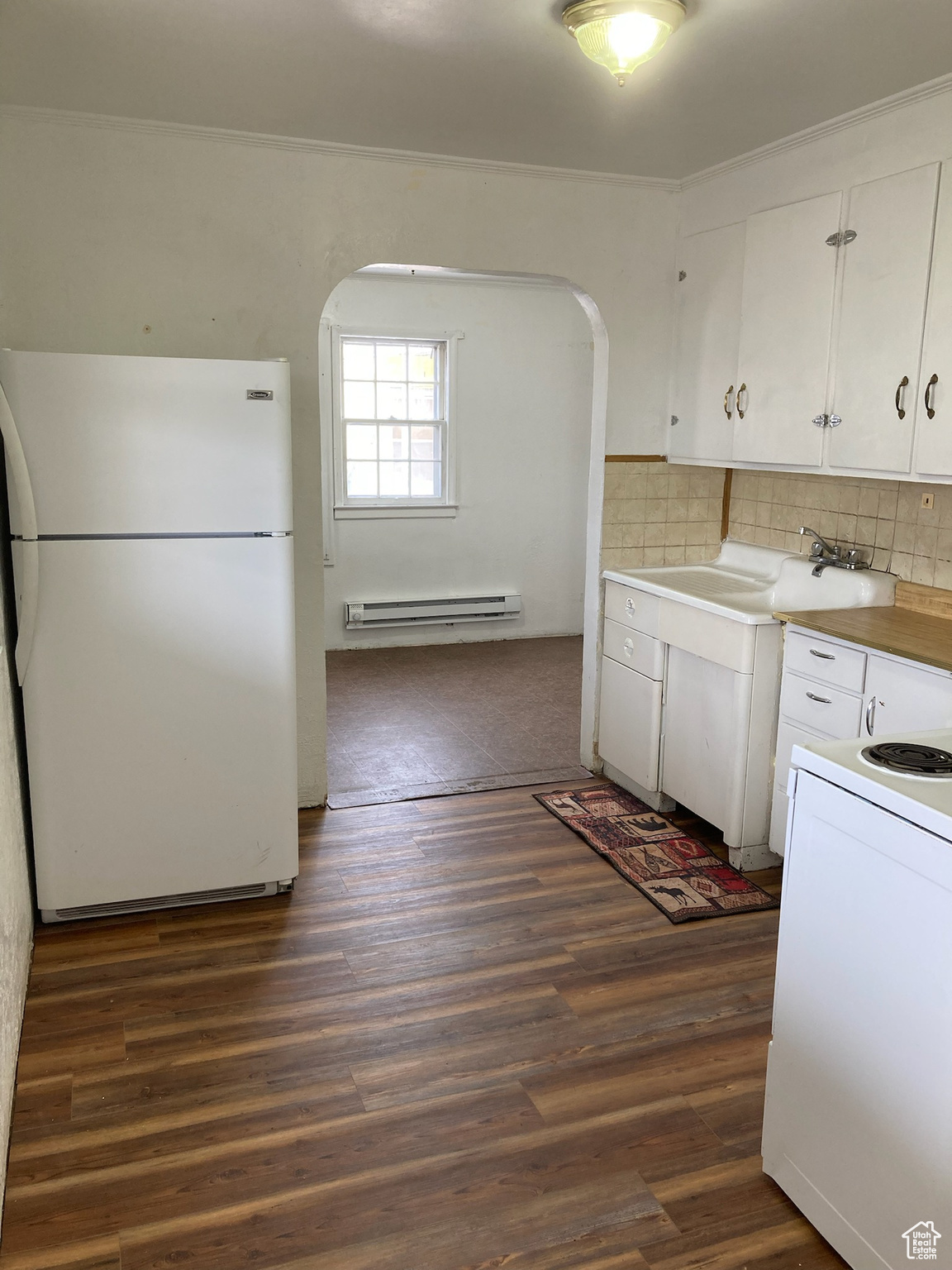 Kitchen featuring white cabinetry, sink, a baseboard radiator, dark hardwood / wood-style flooring, and white appliances