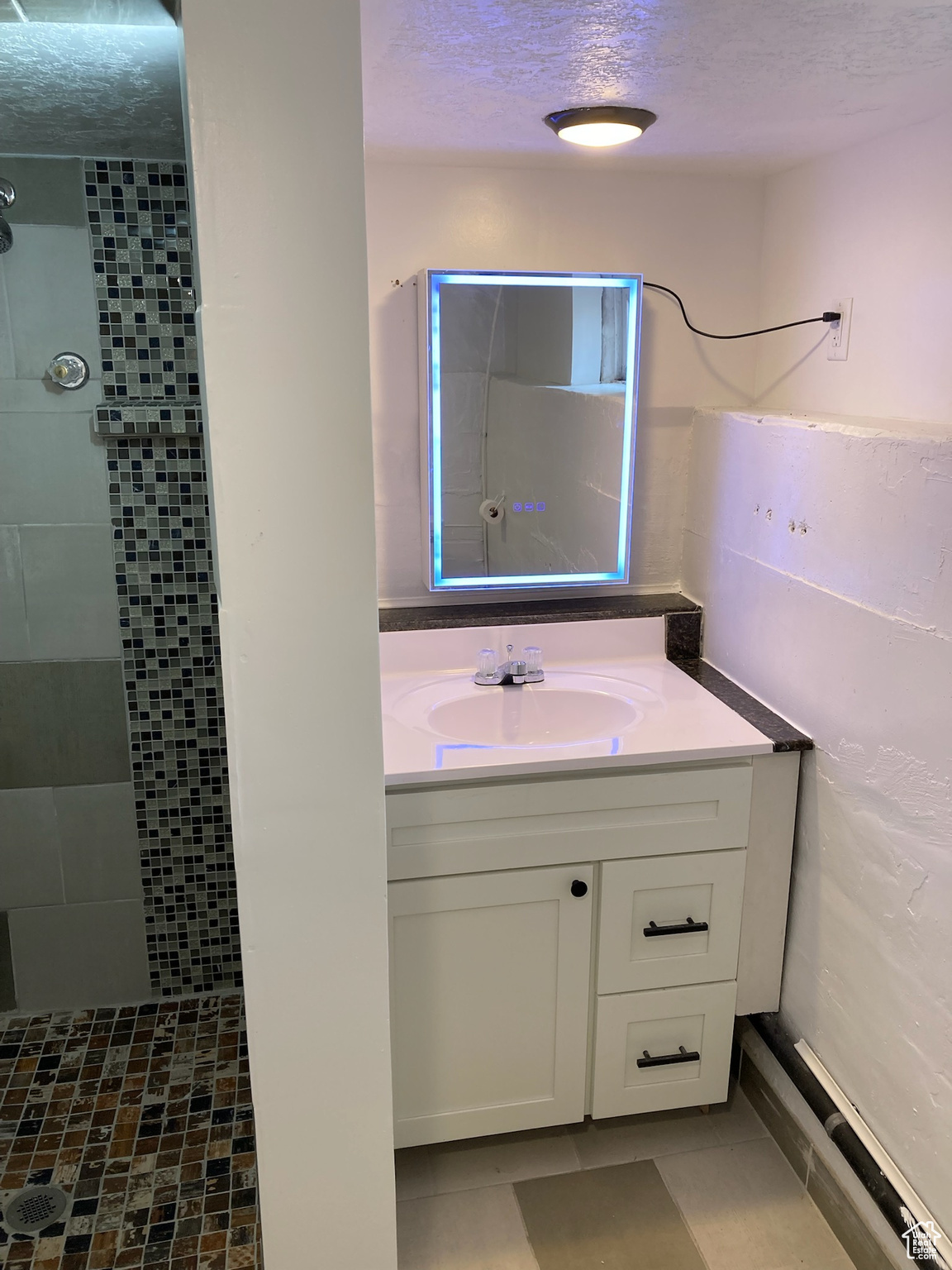 Bathroom with tile patterned flooring, a tile shower, vanity, and a textured ceiling