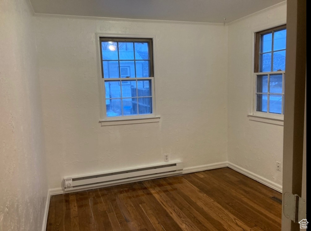 Spare room featuring dark wood-type flooring, ornamental molding, and a baseboard heating unit