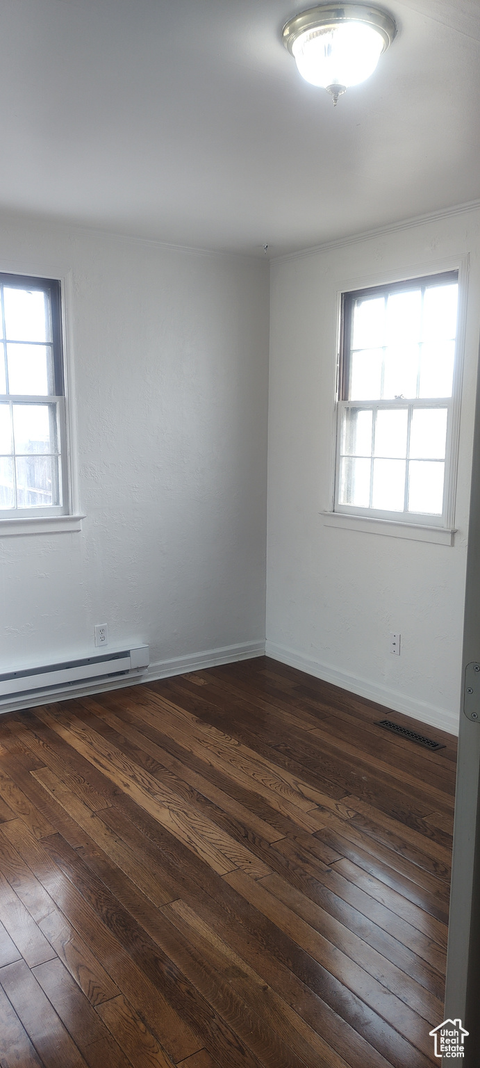 Empty room with dark hardwood / wood-style flooring and baseboard heating