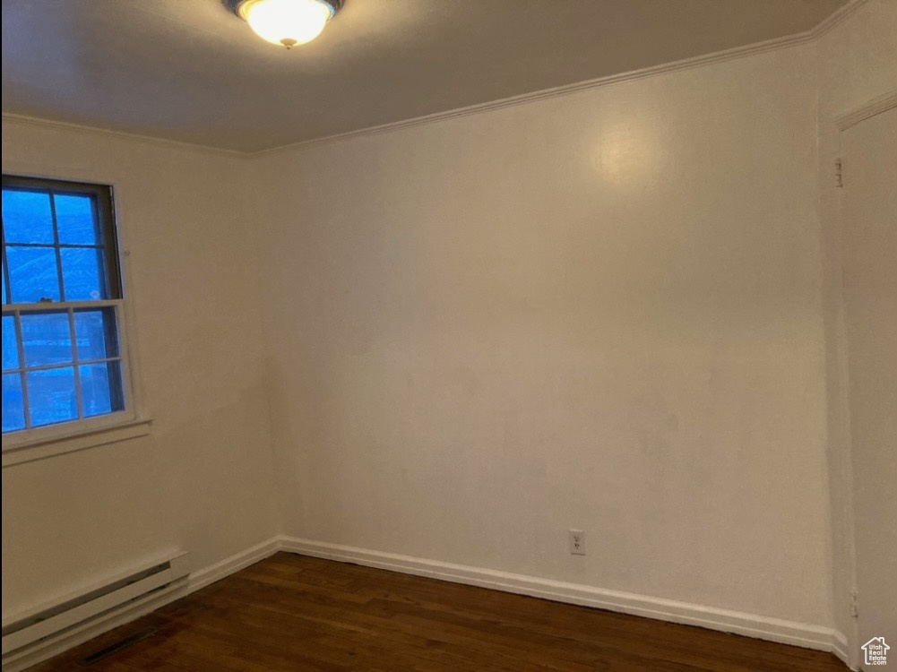 Empty room with crown molding, a baseboard radiator, and dark hardwood / wood-style floors