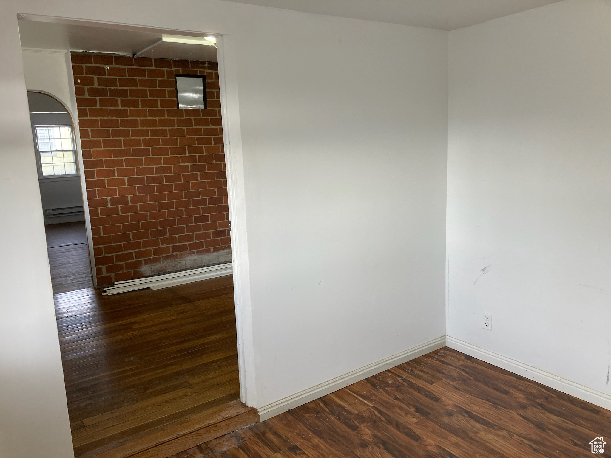 Empty room with dark hardwood / wood-style flooring and a baseboard radiator