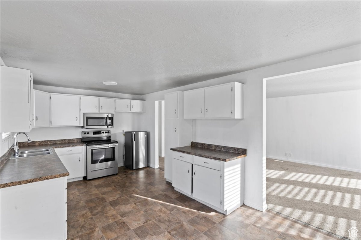 Kitchen with sink, white cabinets, stainless steel appliances, and a textured ceiling