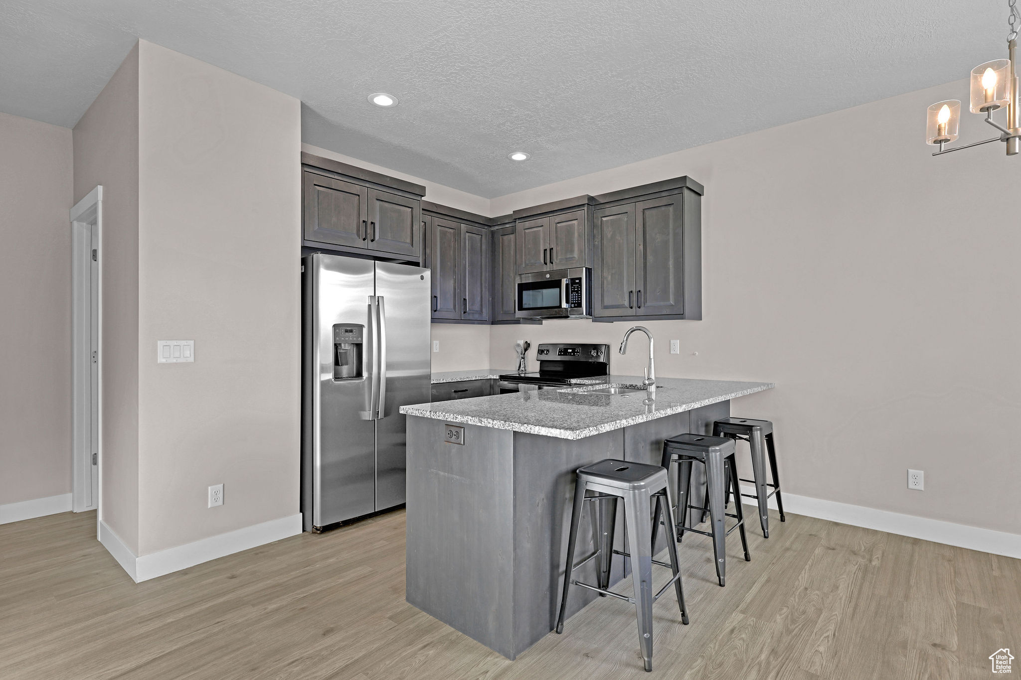 Kitchen with a breakfast bar, sink, a textured ceiling, kitchen peninsula, and stainless steel appliances