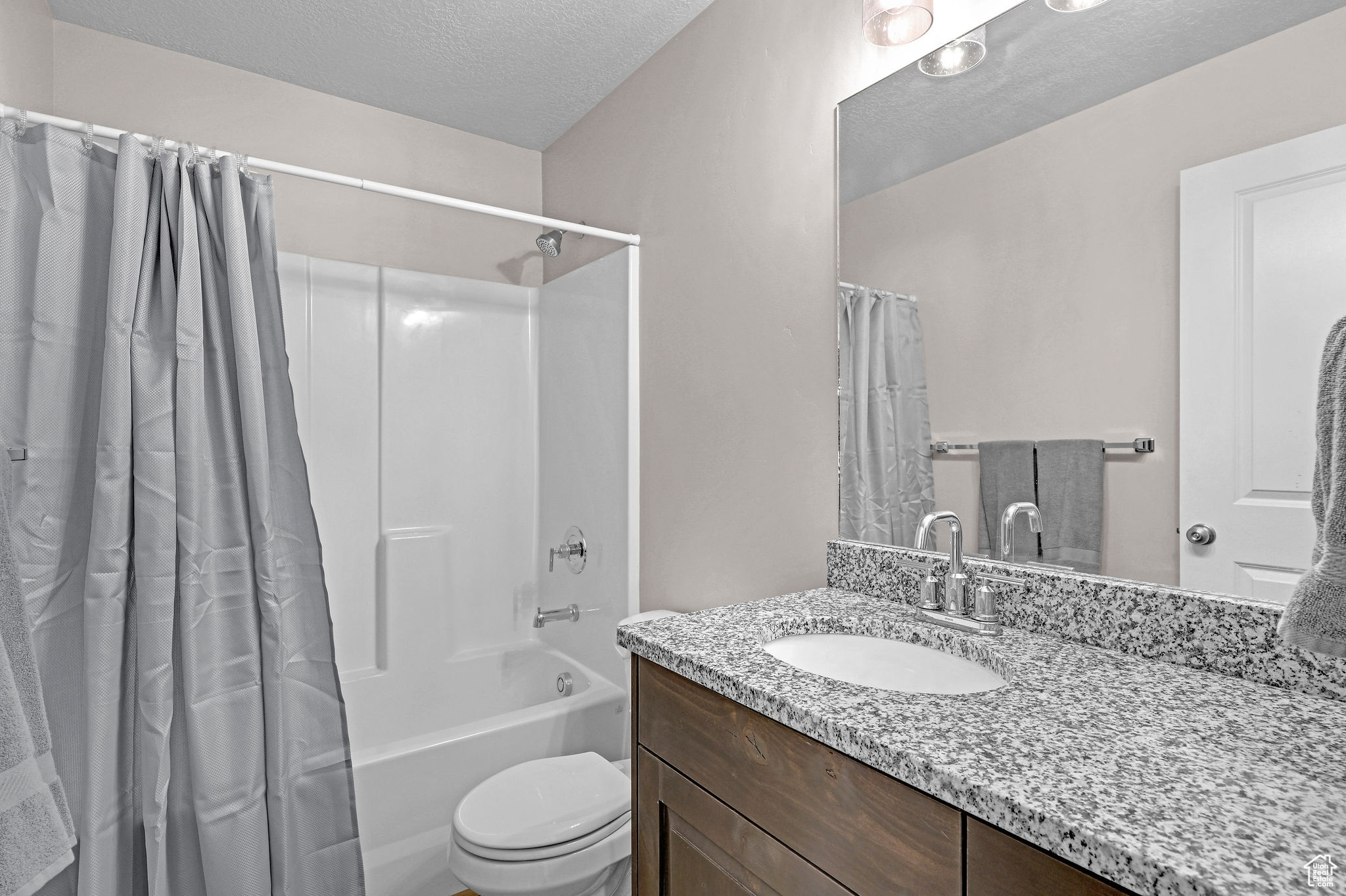 Full bathroom featuring shower / tub combo with curtain, vanity, a textured ceiling, and toilet