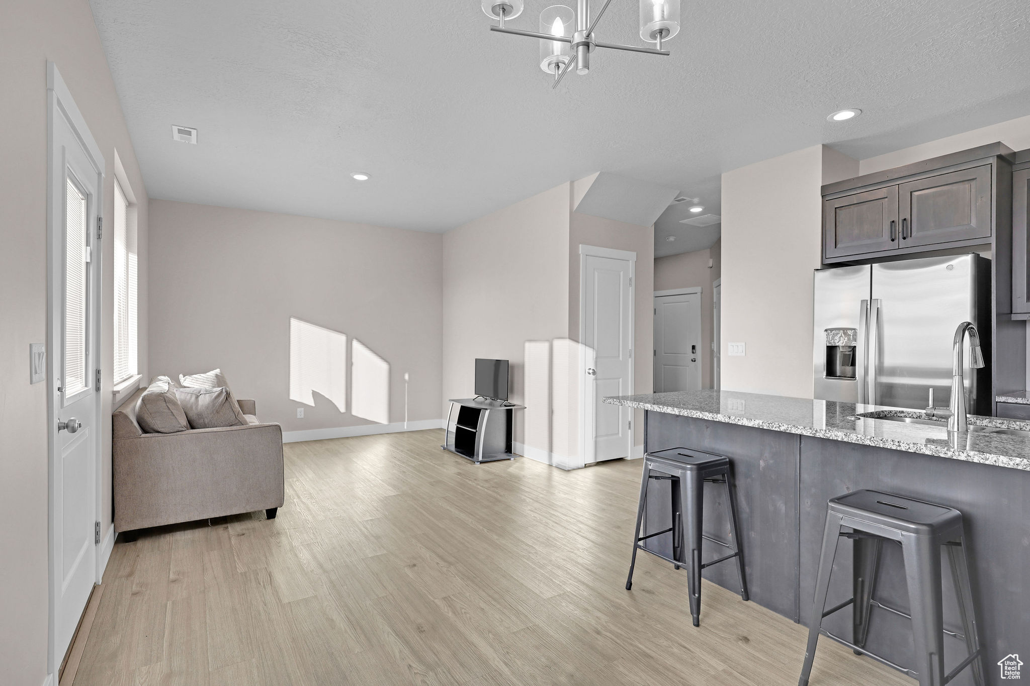 Kitchen with light stone countertops, a breakfast bar, dark brown cabinets, sink, and stainless steel fridge with ice dispenser