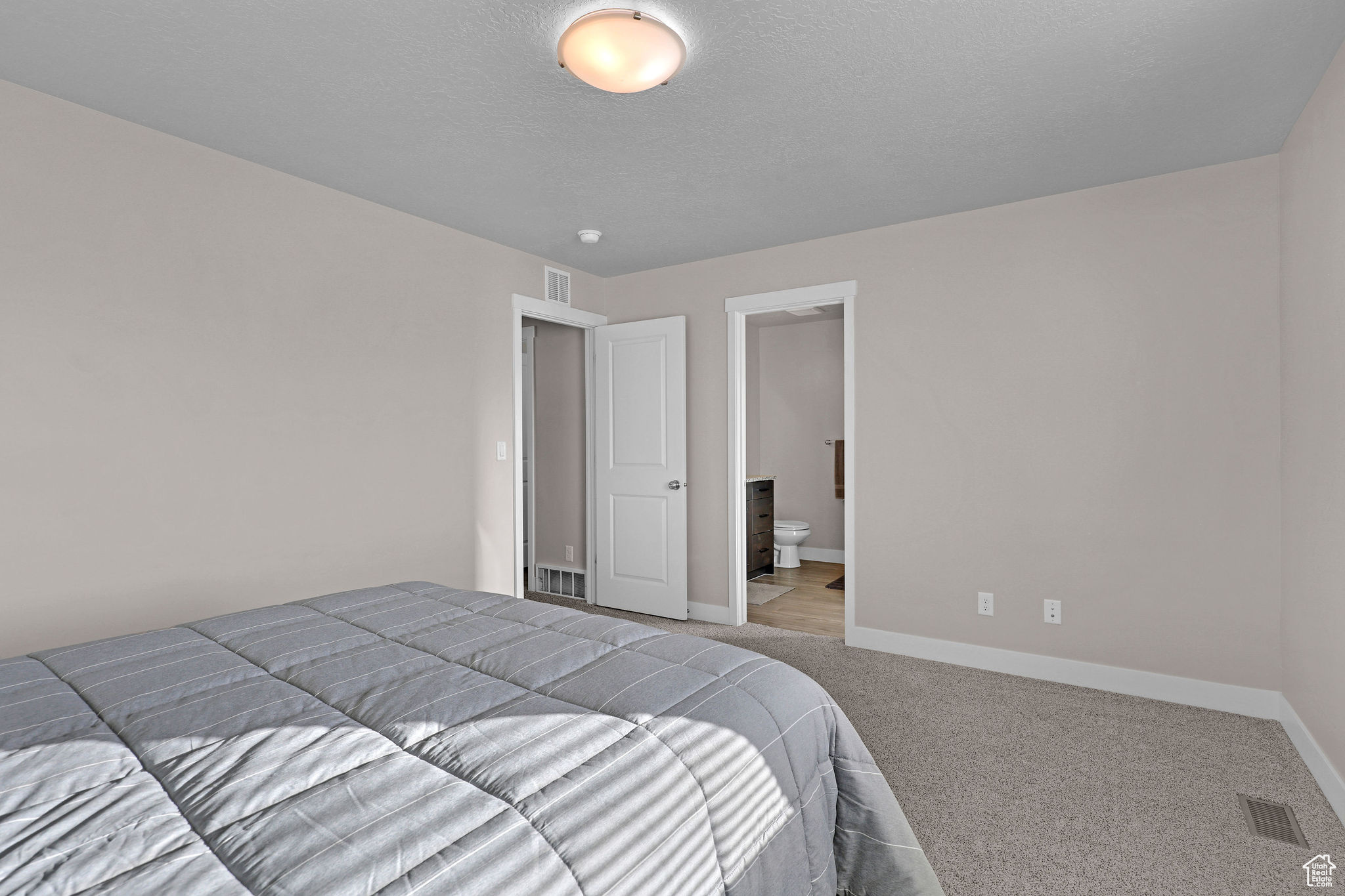 Bedroom featuring a textured ceiling, light colored carpet, and ensuite bath