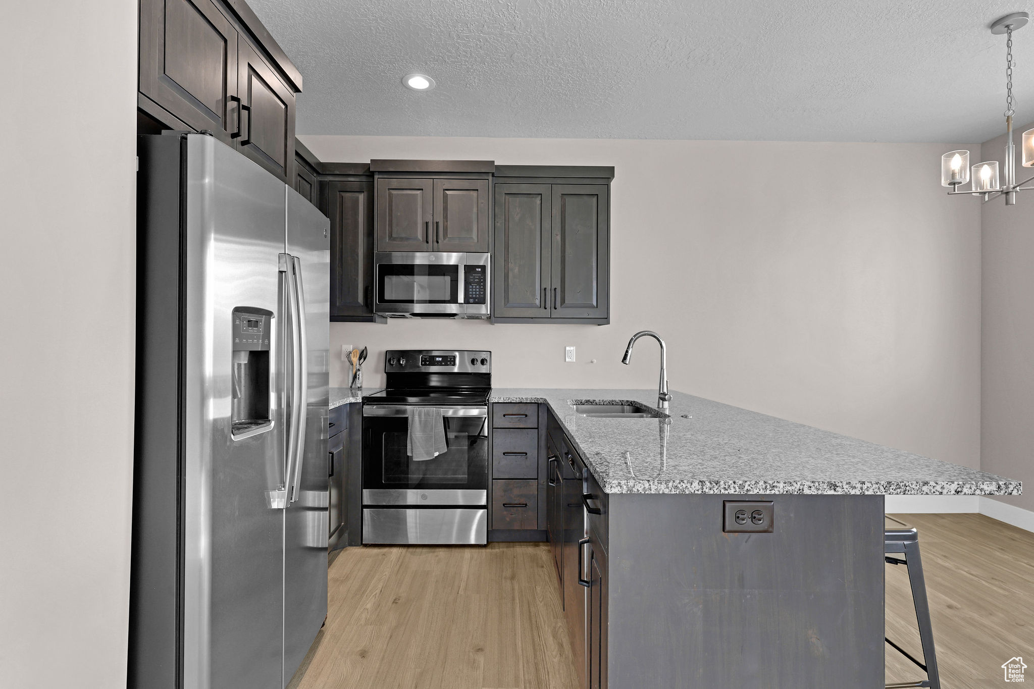 Kitchen with an inviting chandelier, hanging light fixtures, sink, appliances with stainless steel finishes, and a kitchen bar