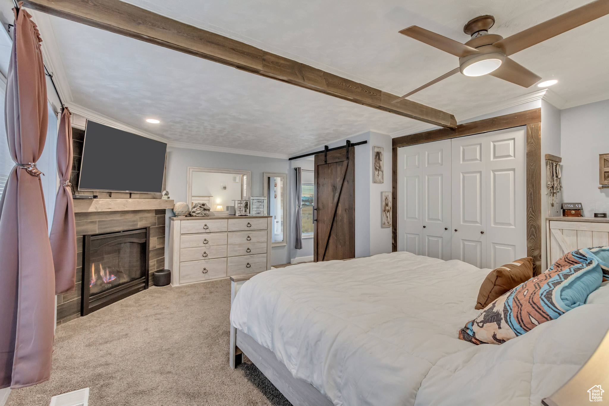 Carpeted bedroom with beam ceiling, ceiling fan, a barn door, a closet, and crown molding