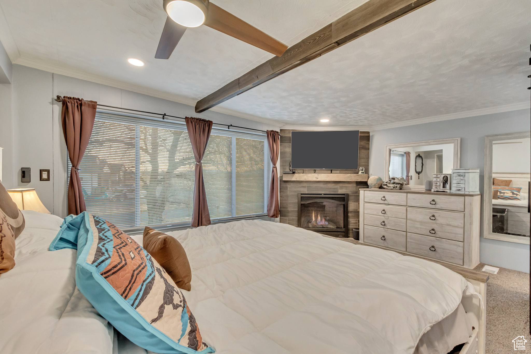 Bedroom featuring beam ceiling, carpet flooring, ceiling fan, a large fireplace, large windows and crown molding