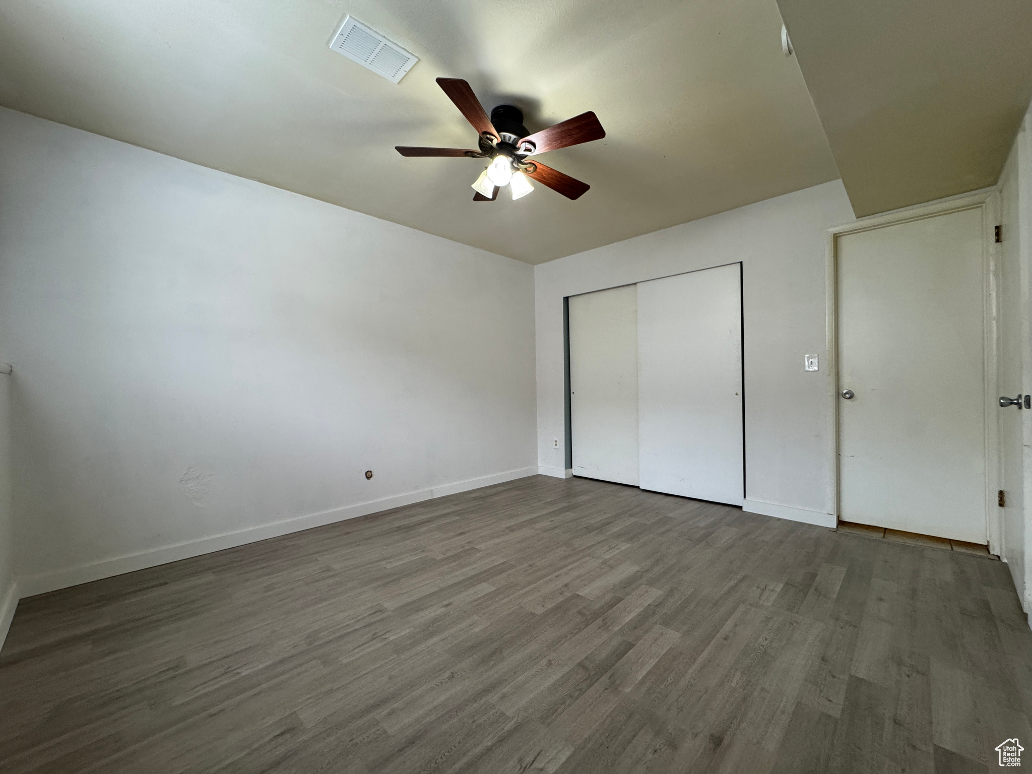 Unfurnished bedroom featuring hardwood / wood-style floors, a closet, and ceiling fan