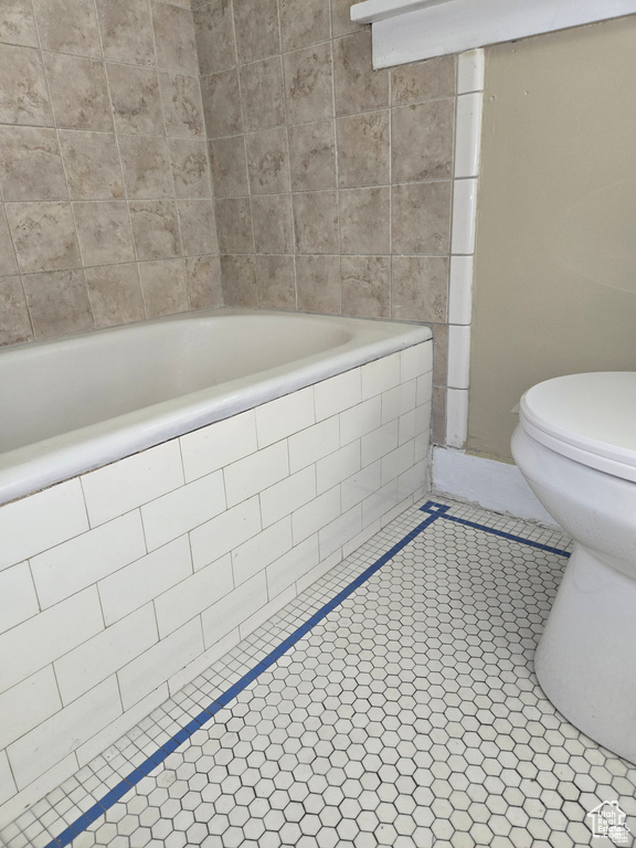 Bathroom featuring tile patterned floors, tiled bath, and toilet