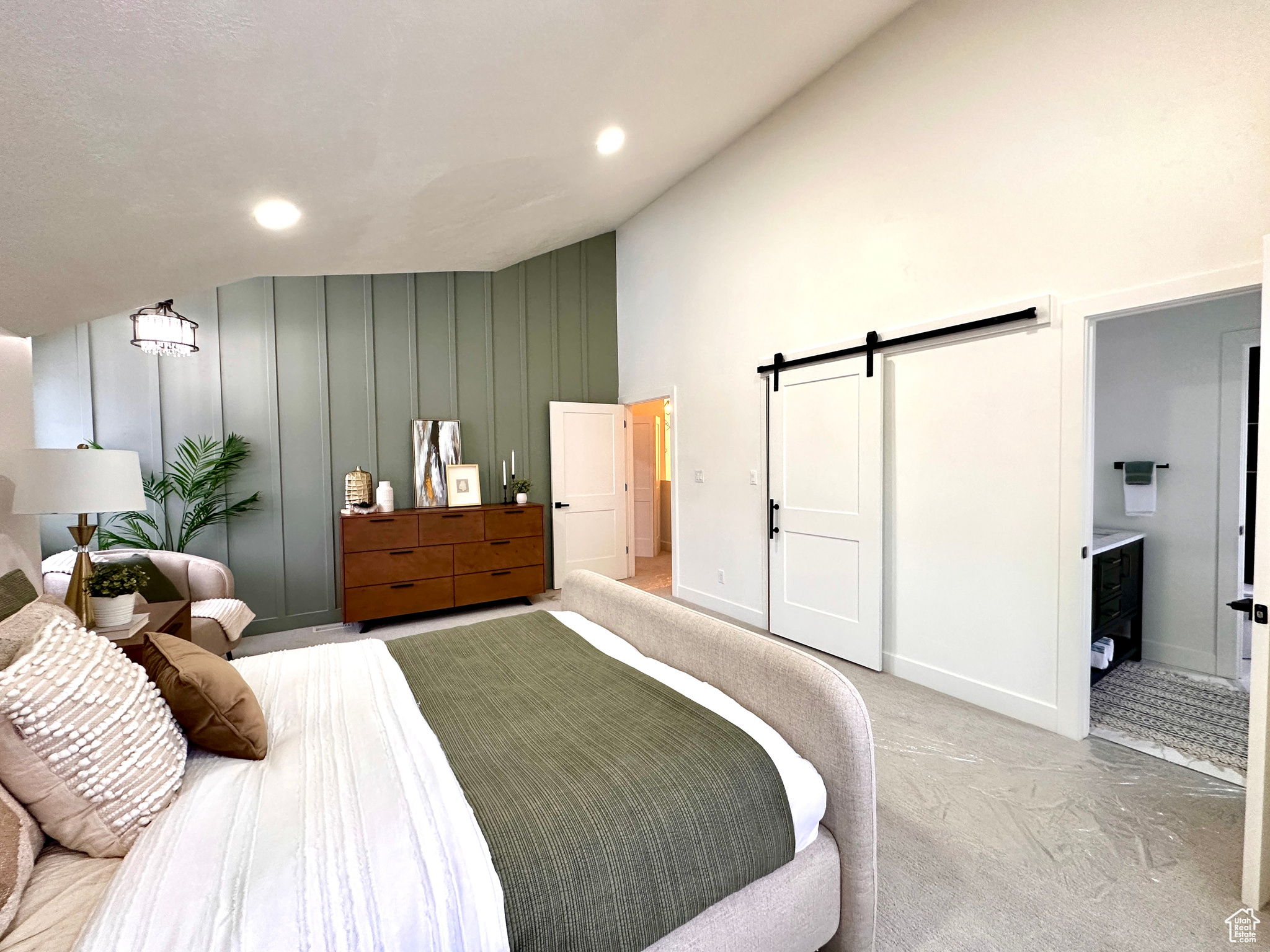 Bedroom with light carpet, a barn door, ensuite bath, and vaulted ceiling