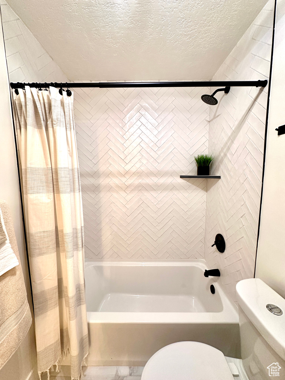 Bathroom featuring shower / bath combo, a textured ceiling, and toilet