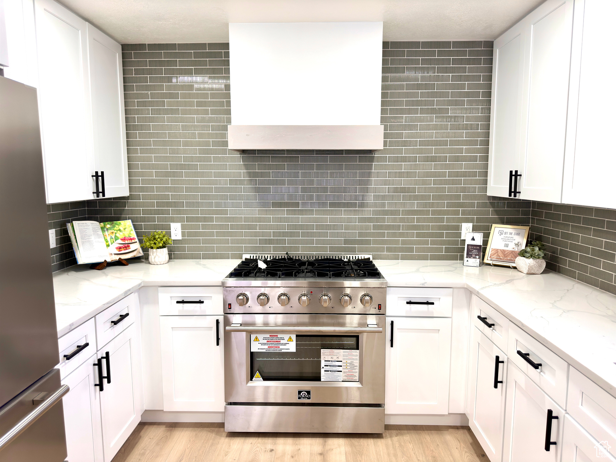 Kitchen featuring exhaust hood, decorative backsplash, white cabinets, and stainless steel appliances