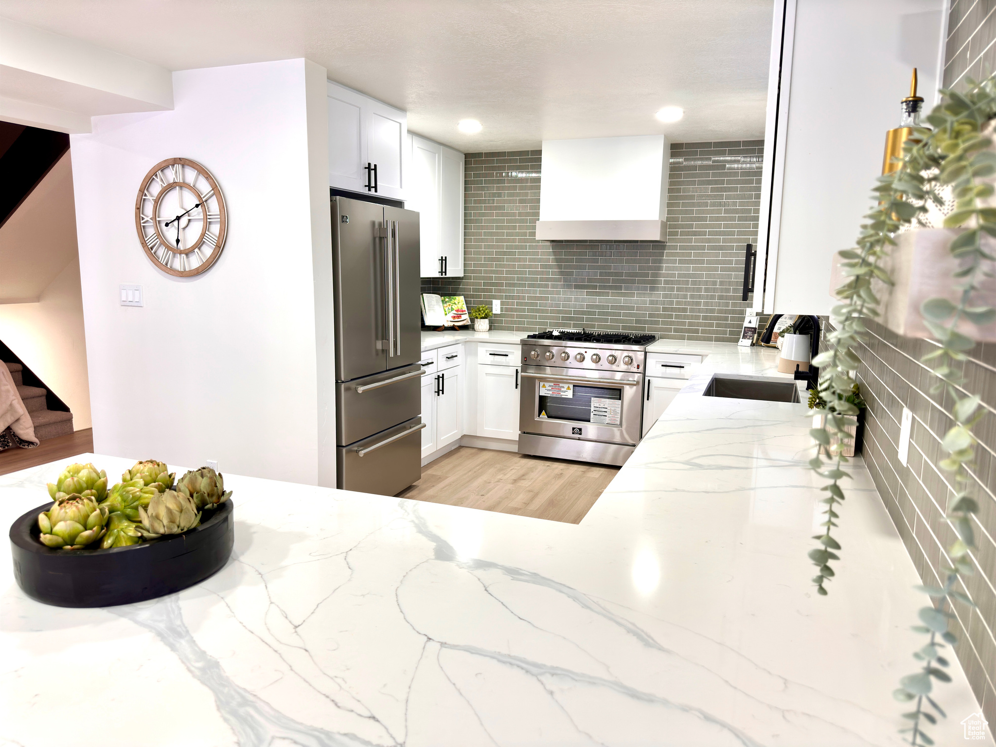 Kitchen with decorative backsplash, high quality appliances, white cabinets, and wall chimney range hood